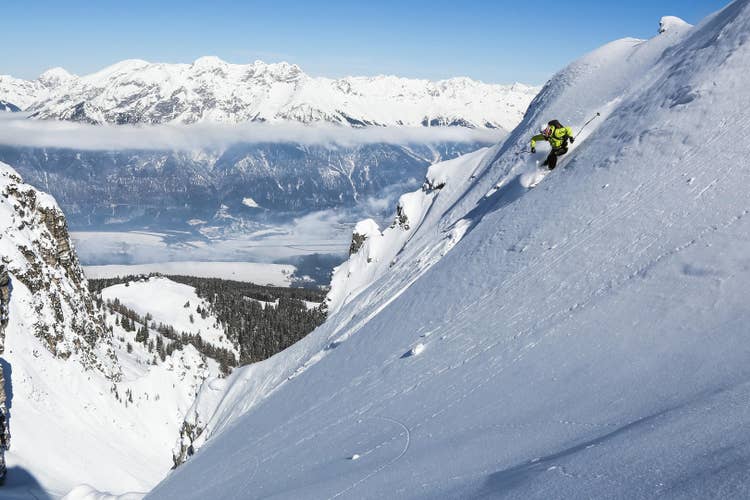 Steep freeride skiing above a valley — terrain where the commitment to line selection happens before the edge tips, not a moment after