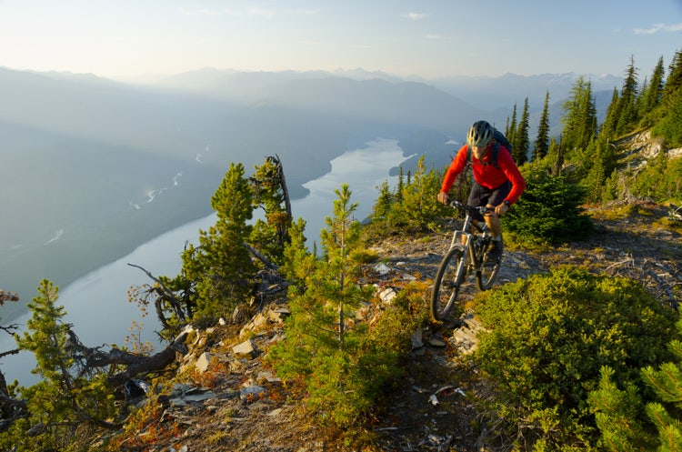 A mountain biker riding high above the valley in the Purcell Mountains — above the treeline, the world shrinks to the trail, the bike, and the distance to the next ridge