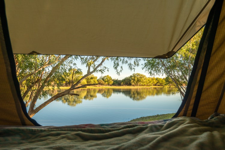 View from a tent doorway over a remote billabong, Northern Territory — the desert night that drops 20°C after sunset, demanding the emergency bivy you almost didn