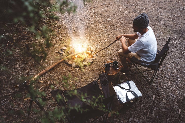 A hiker settled by a campfire in the forest after a long day in the wind — one of the better reasons to carry an Aeropress all the way to Patagonia, even if it adds 200g